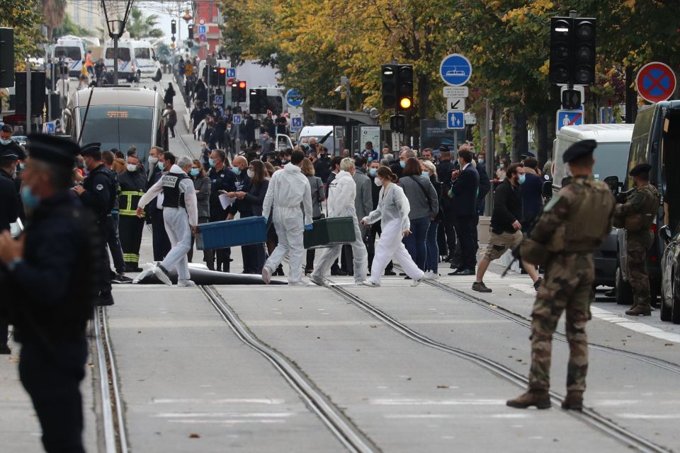 Forensics officers deploy stretchers at the site of a knife attack as French soldiers stand guard the street in Nice