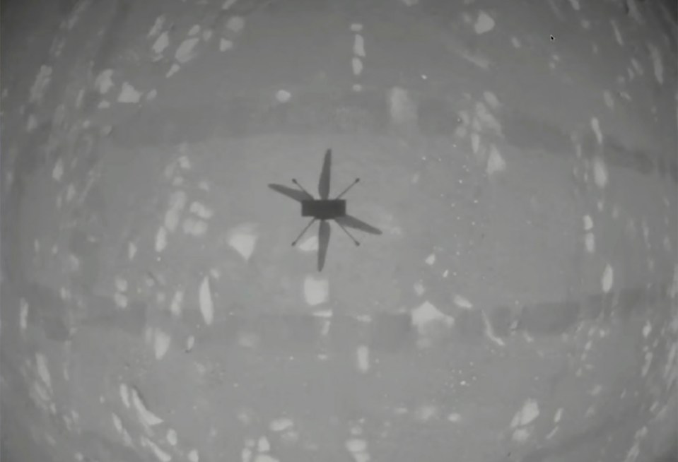 Ingenuity hovers above Mars during the first powered flight carried out on another planet. The image is a point of view from the drone, with its shadow cast onto the surface below
