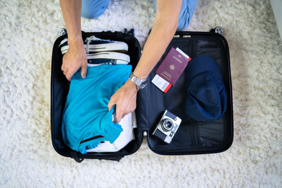 a person is packing a suitcase with a passport and a camera