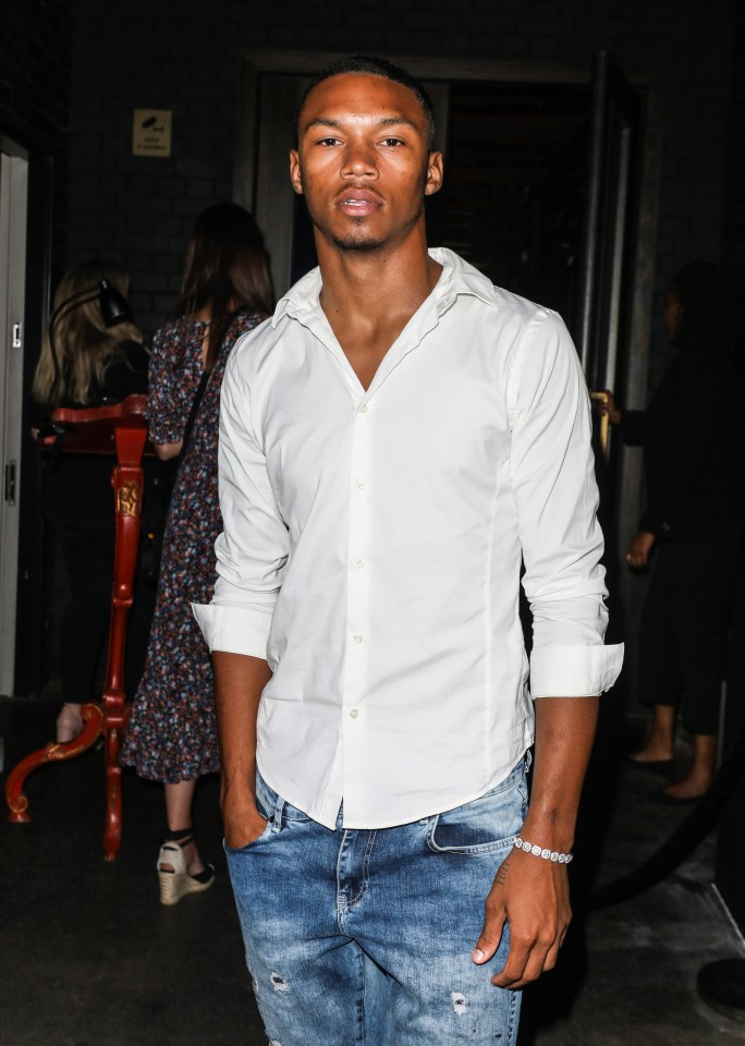 a man wearing a white shirt and blue jeans stands in front of a door