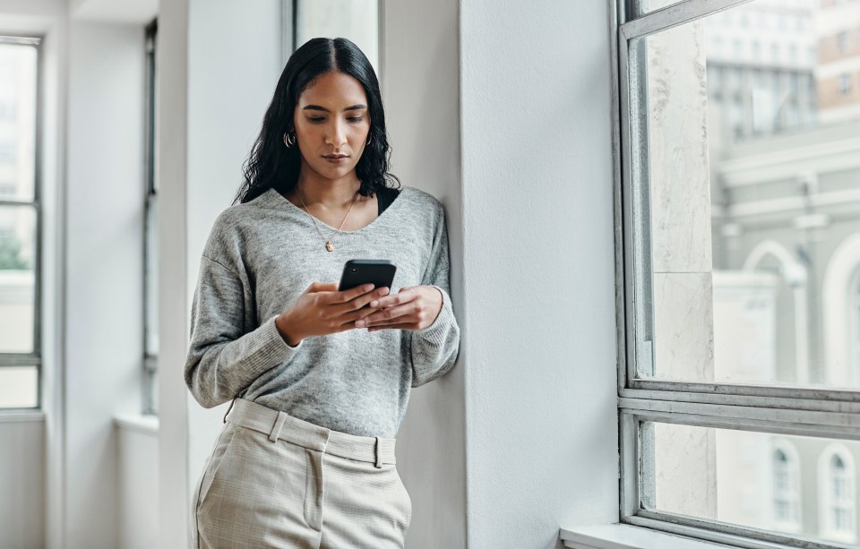 a woman leaning against a wall looking at her phone