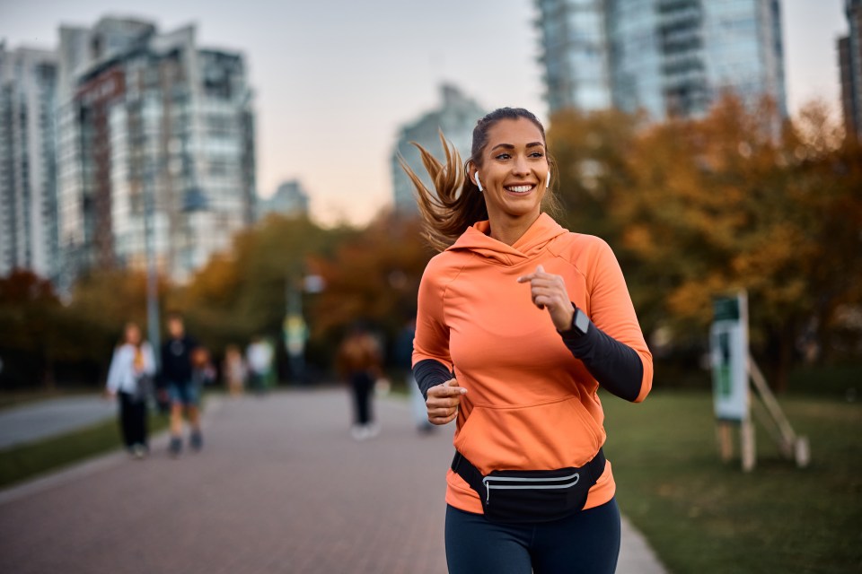 a woman in an orange hoodie is running down a path