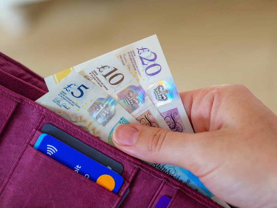 Hand taking British money from a wallet.