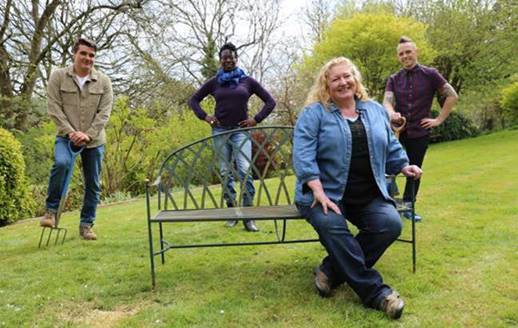 a group of people are standing around a bench in a garden .