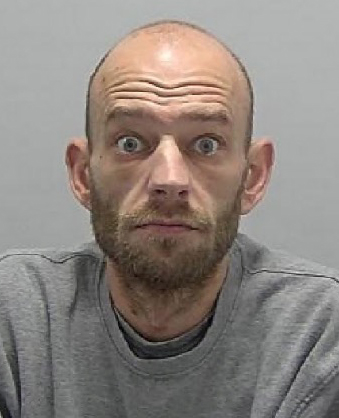 a bald man with a beard is wearing a grey sweater and making a funny face .