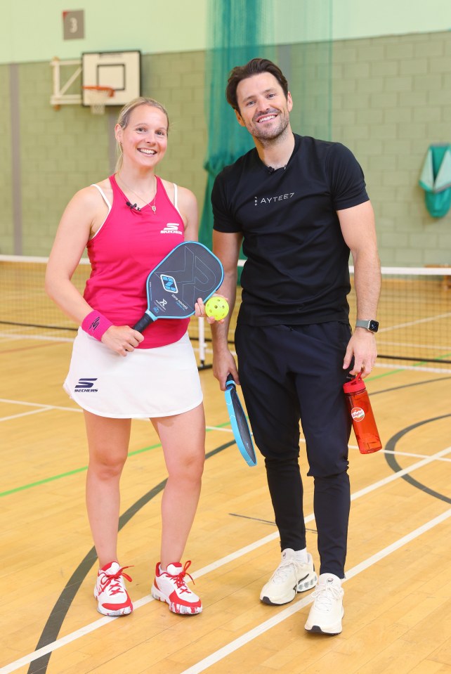 a man wearing a aytree shirt stands next to a woman holding a paddle