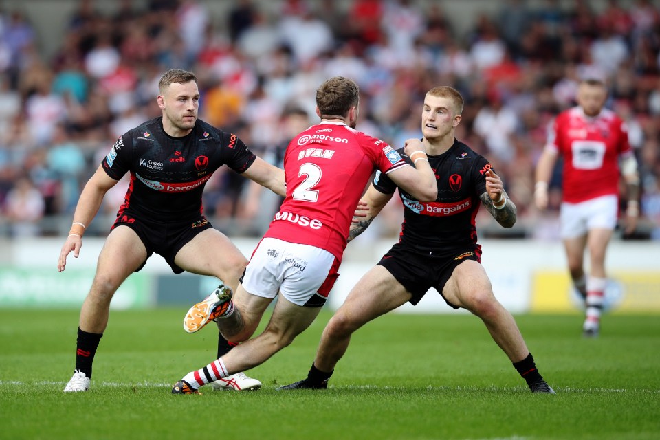 Salford Red Devils' Ethan Ryan is challenged by St.Helens' Matty Lees (L) and George Delaney during the Betfred Super League match at the Salford Community Stadium, Salford. Picture date: Sunday June 23, 2024. PA Photo. See PA story RUGBYL Salford. Photo credit should read: Jessica Hornby/PA Wire. RESTRICTIONS: Use subject to restrictions. Editorial use only, no commercial use without prior consent from rights holder.
