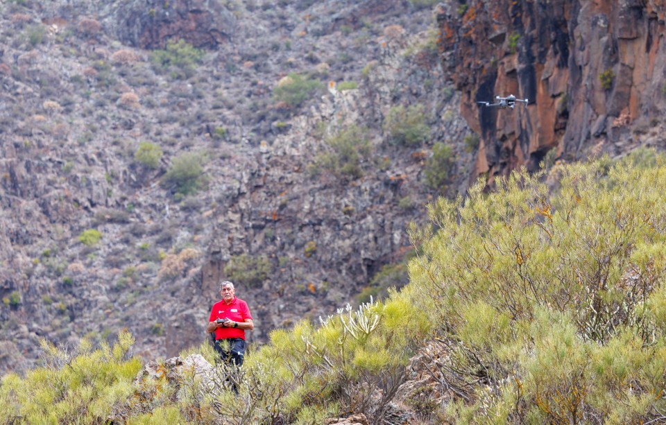a man in a red shirt is standing in a field with a drone in the background