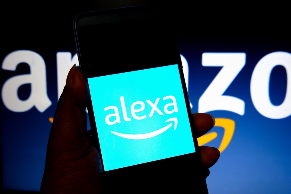 Photo illustration of a smartphone displaying the Alexa logo against a blurred Amazon logo background.