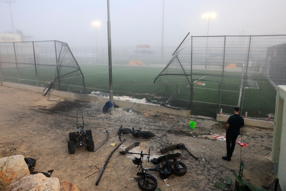 A man stands near a damaged gate around a football pitch after a reported strike from Lebanon fell in Majdal Shams village in the Israeli-annexed Golan area on July 28, 2024. Israel's military said Hezbollah fired the rocket from Lebanon, hitting a football pitch in the Druze town of Majdal Shams and killing the youngsters, who were between 10 and 20 years old. Another 18 youths were wounded in the attack, said the emergency services. (Photo by Menahem Kahana / AFP) (Photo by MENAHEM KAHANA/AFP via Getty Images)
