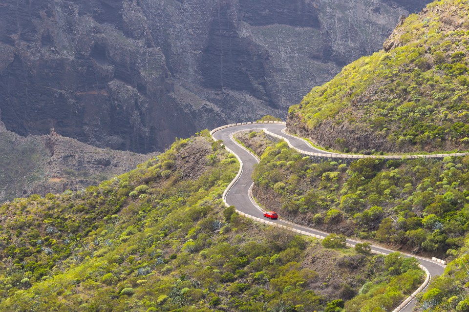 a red car is driving down a winding mountain road
