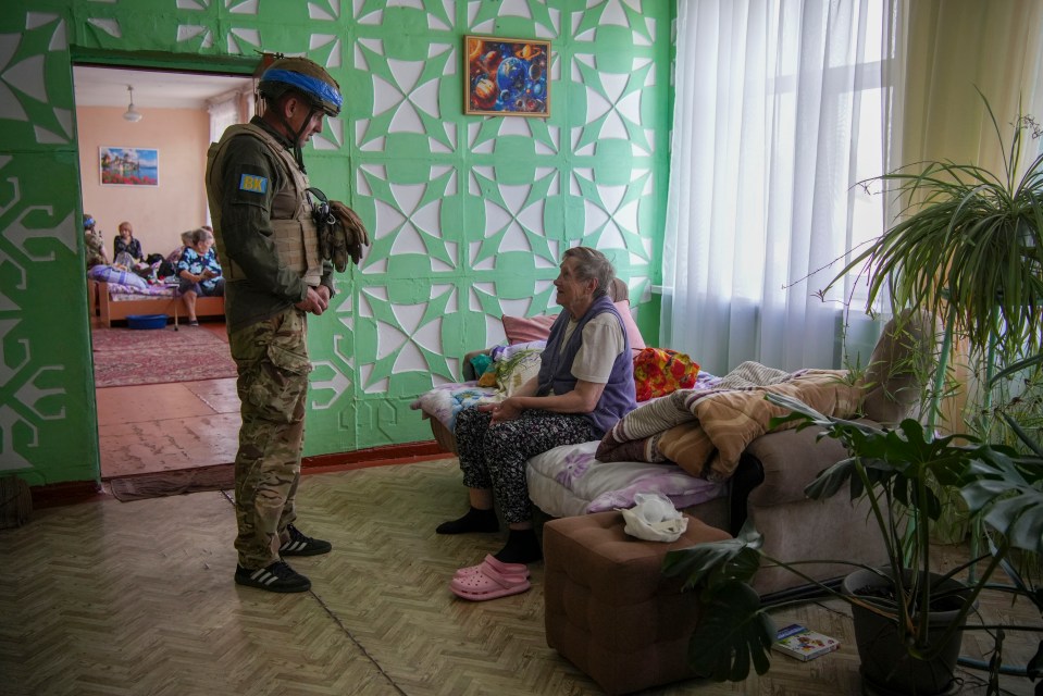 a soldier talks to an elderly woman sitting on a couch
