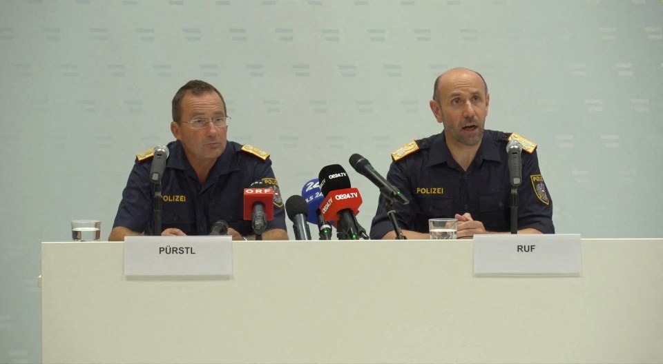 two police officers are sitting at a table with microphones and a sign that says purstl