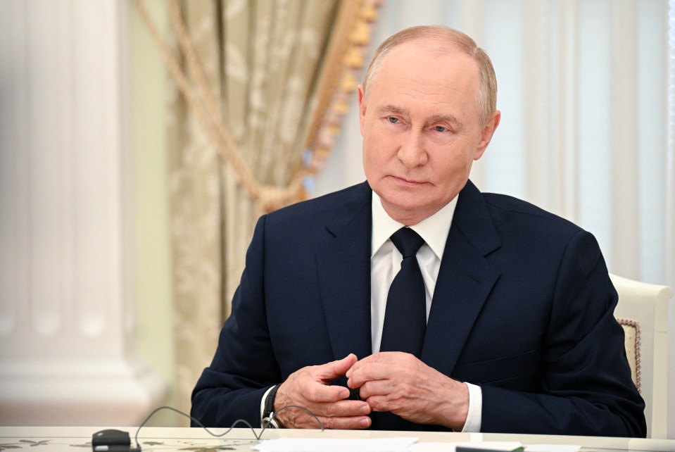a man in a suit and tie sits at a desk with his hands folded