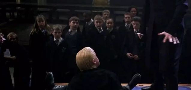 a group of children are standing around a boy laying on the floor .