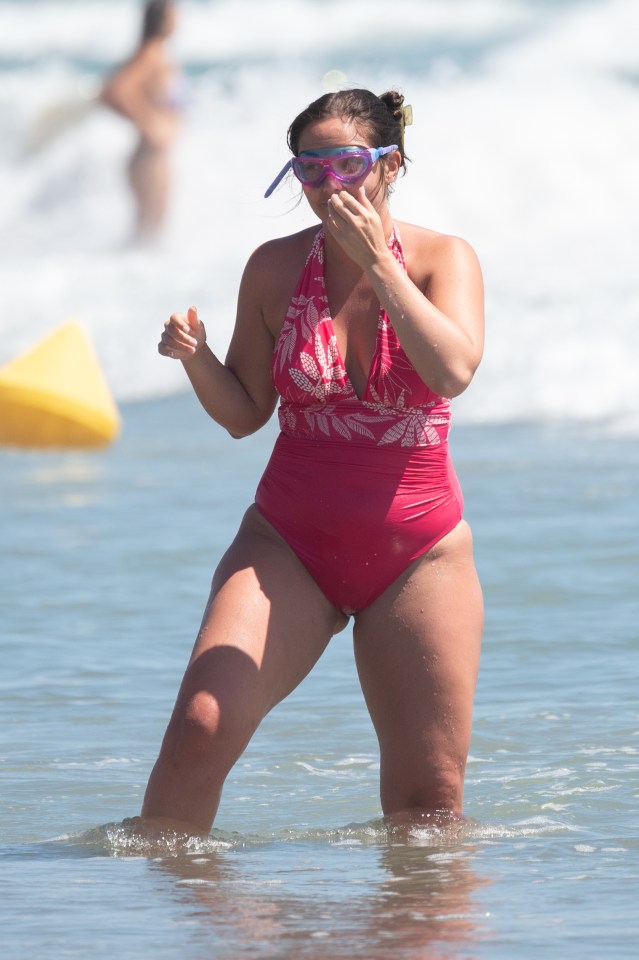 a woman in a pink swimsuit and goggles stands in the water