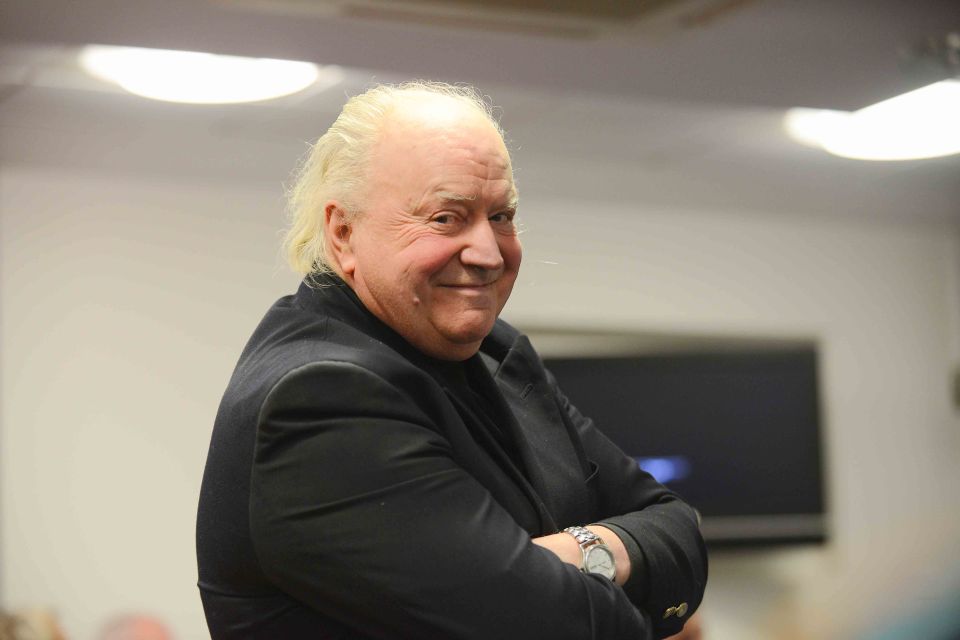 a man with white hair wearing a black jacket and a watch