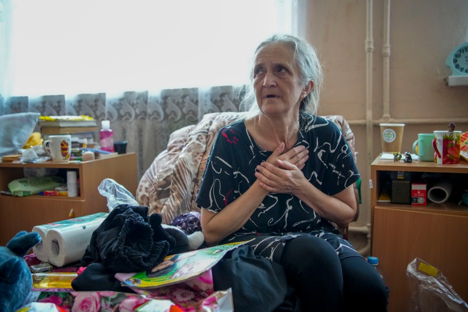 an elderly woman sits on a bed with a clock on the wall that says 10:08