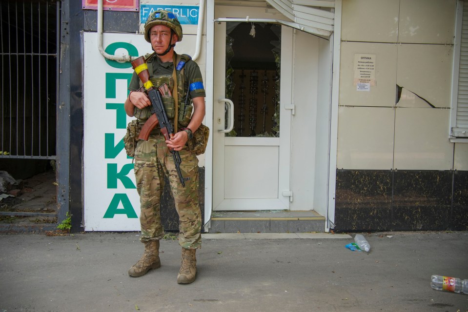 A Ukrainian soldier patrols in Sudzha Main Square outside an optician’s damaged shop