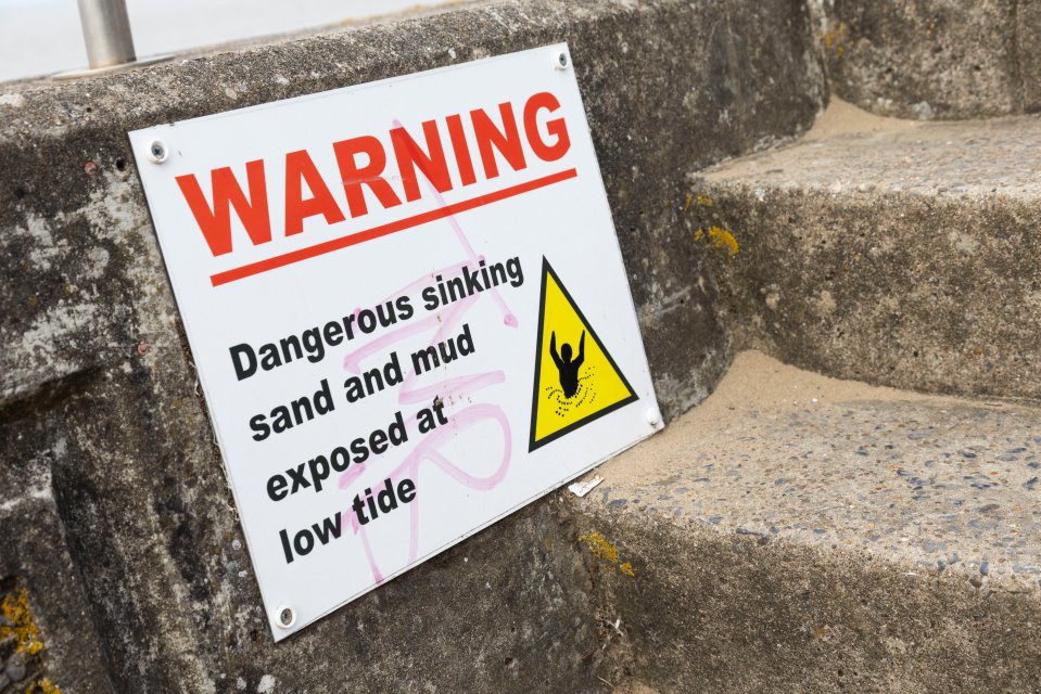 a warning sign that says dangerous sinking sand and mud exposed at low tide