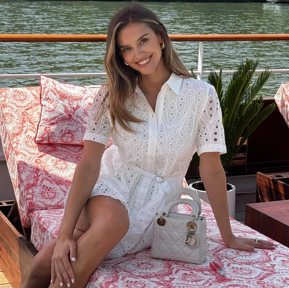 a woman in a white dress sits on a couch next to a dior bag