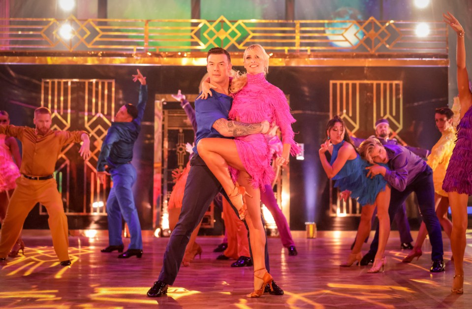 a man in a blue shirt is holding a woman in a pink dress on a dance floor