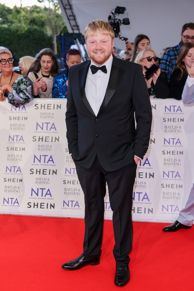 a man in a tuxedo stands in front of a wall that says shein