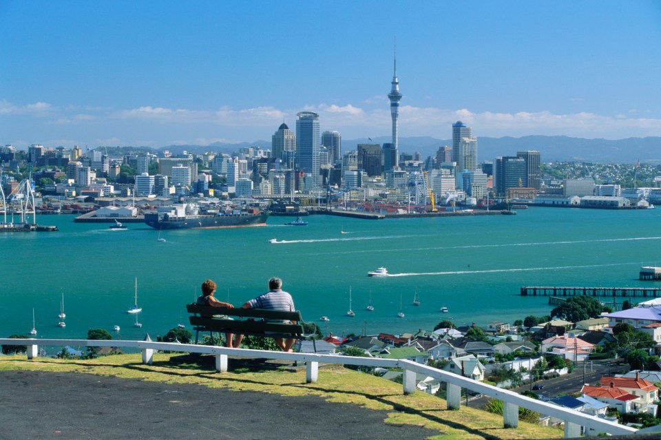 a couple sits on a bench overlooking a city and a body of water