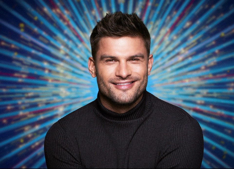 a man in a black turtleneck smiles in front of a blue background