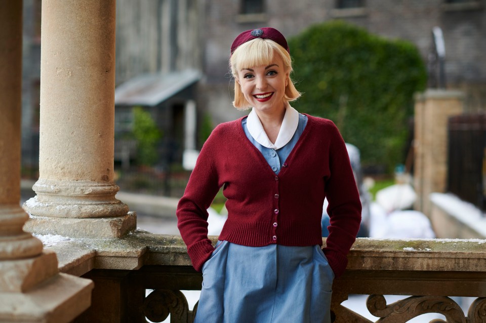 a woman in a red cardigan and blue skirt stands on a balcony