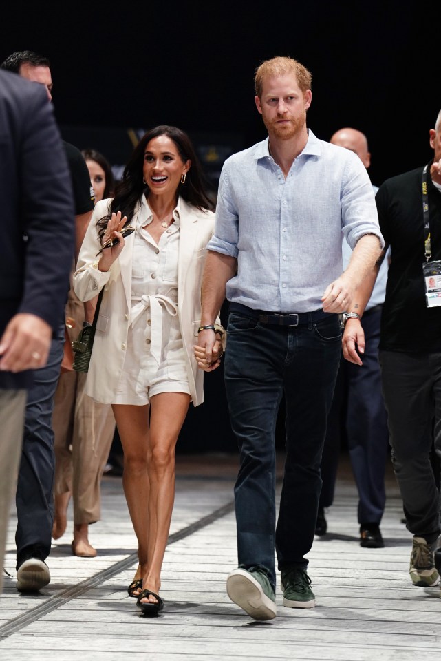 prince harry and meghan markle walk down a street holding hands