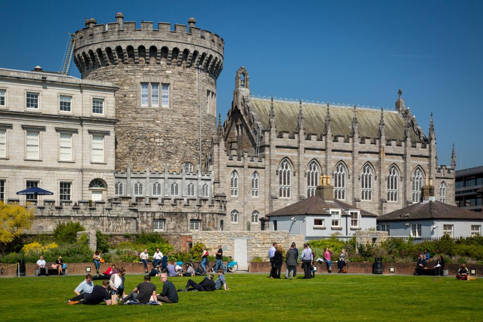 a group of people sit on the grass in front of a castle