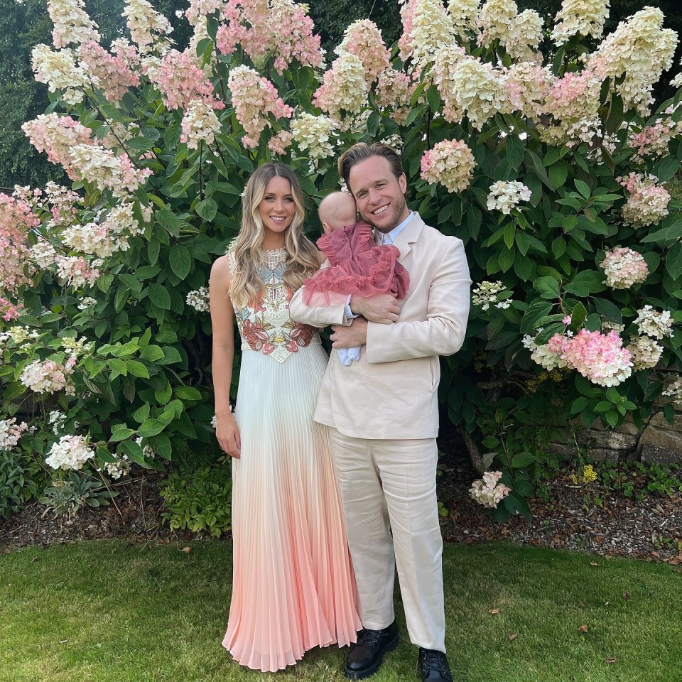 a man and woman holding a baby in front of flowers