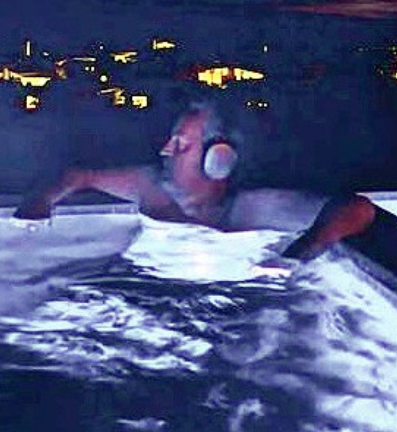 a man is laying in a hot tub wearing headphones .