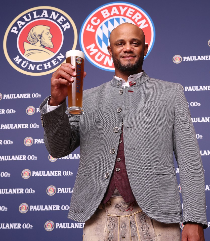 a man holds a glass of beer in front of a paulaner munchen logo