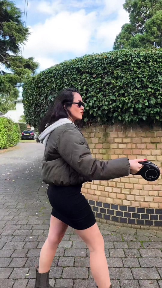 a woman wearing a black skirt and a green jacket is walking down a sidewalk