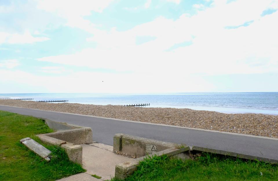 a concrete walkway leading to a beach with a warning sign on it