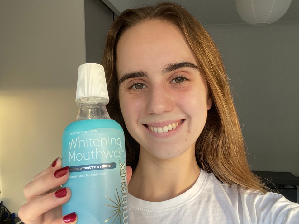 a woman is holding a bottle of whitening mouthwash