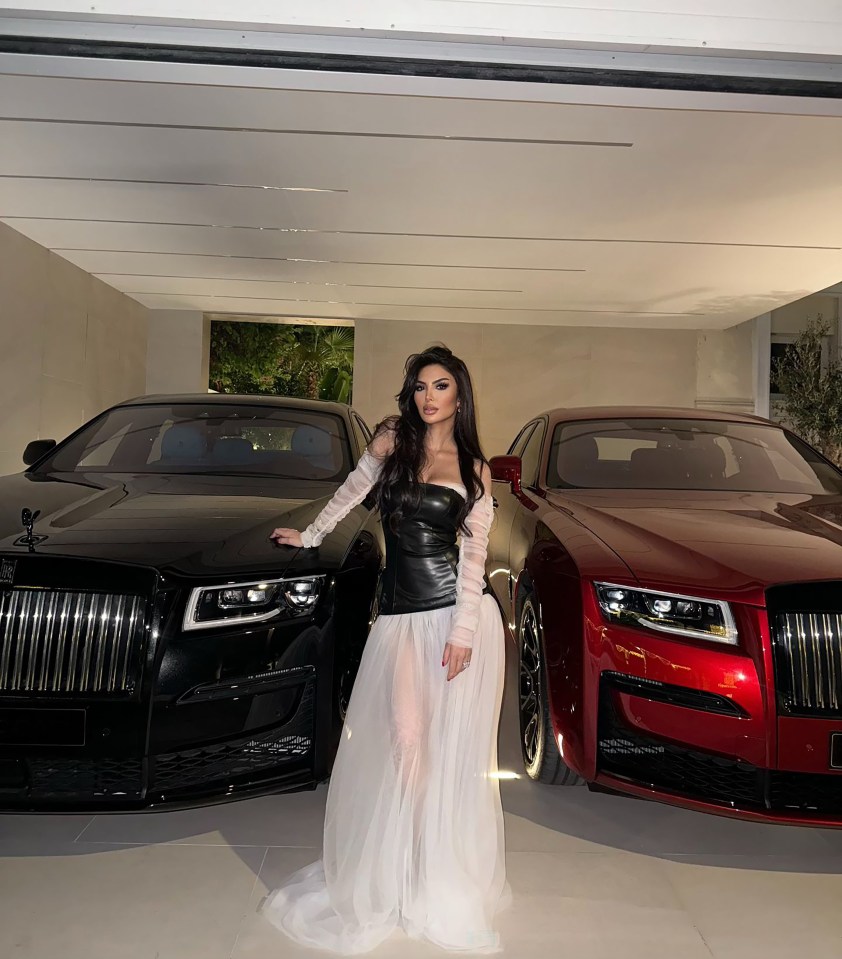 a woman in a white dress stands in front of two rolls royce cars