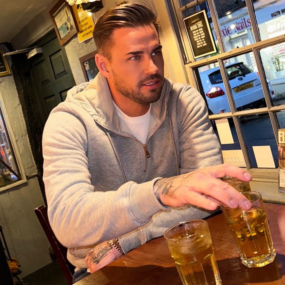 a man sits at a table with two glasses of beer in front of a sign that says cocktails