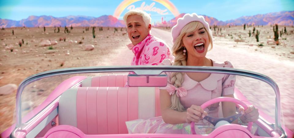 a man and a woman in a pink car with a barbie sign in the background