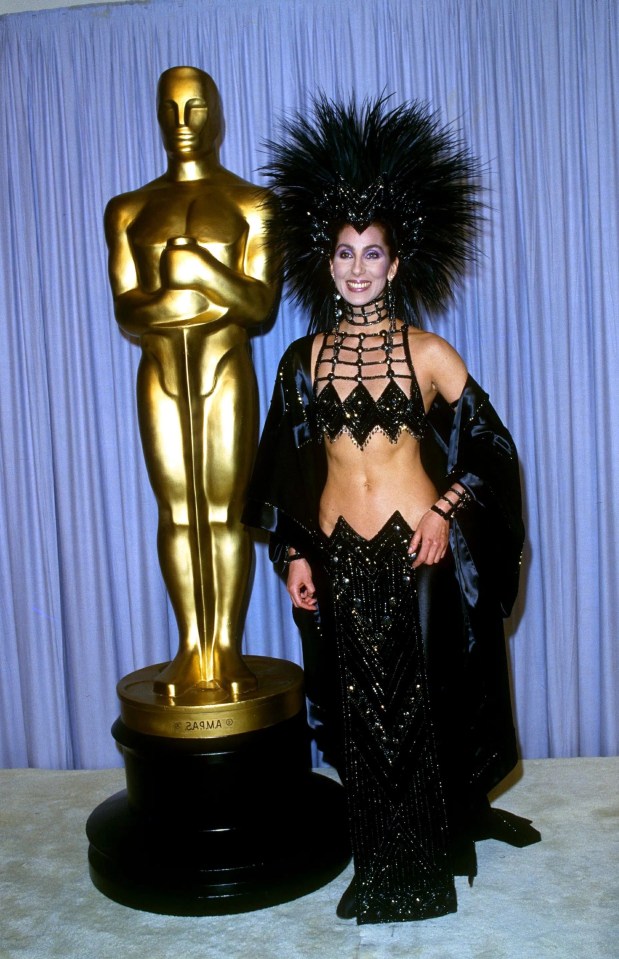 a woman in a black dress stands next to an oscar statue