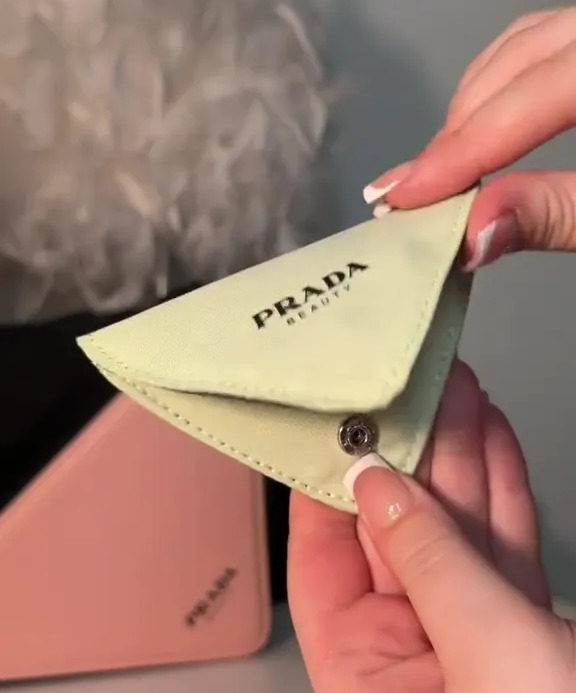 a person is holding a small prada purse in their hand