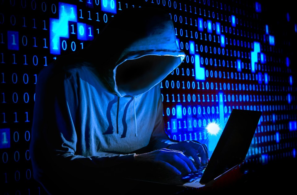 a person in a hoodie is typing on a laptop in front of a wall of binary code