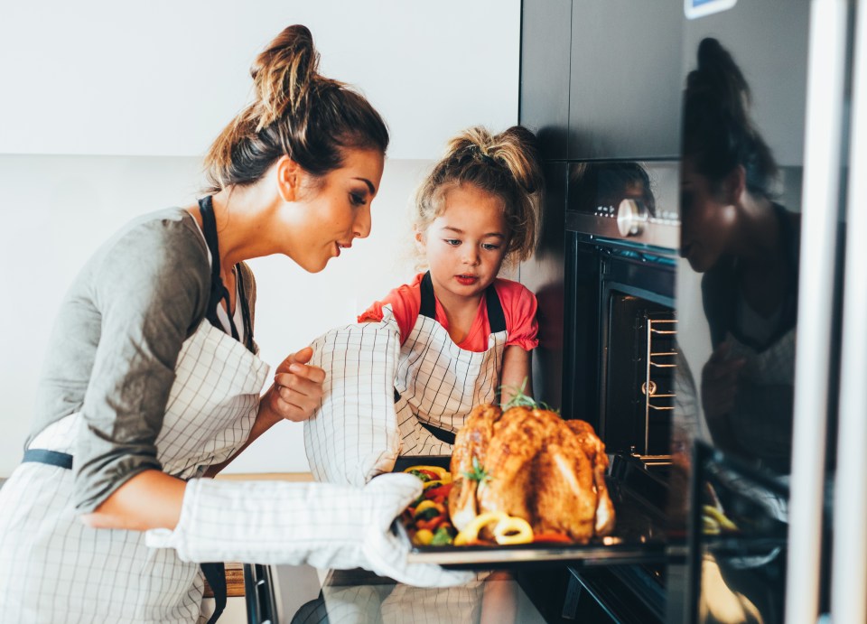 a woman and a little girl are taking a turkey out of the oven