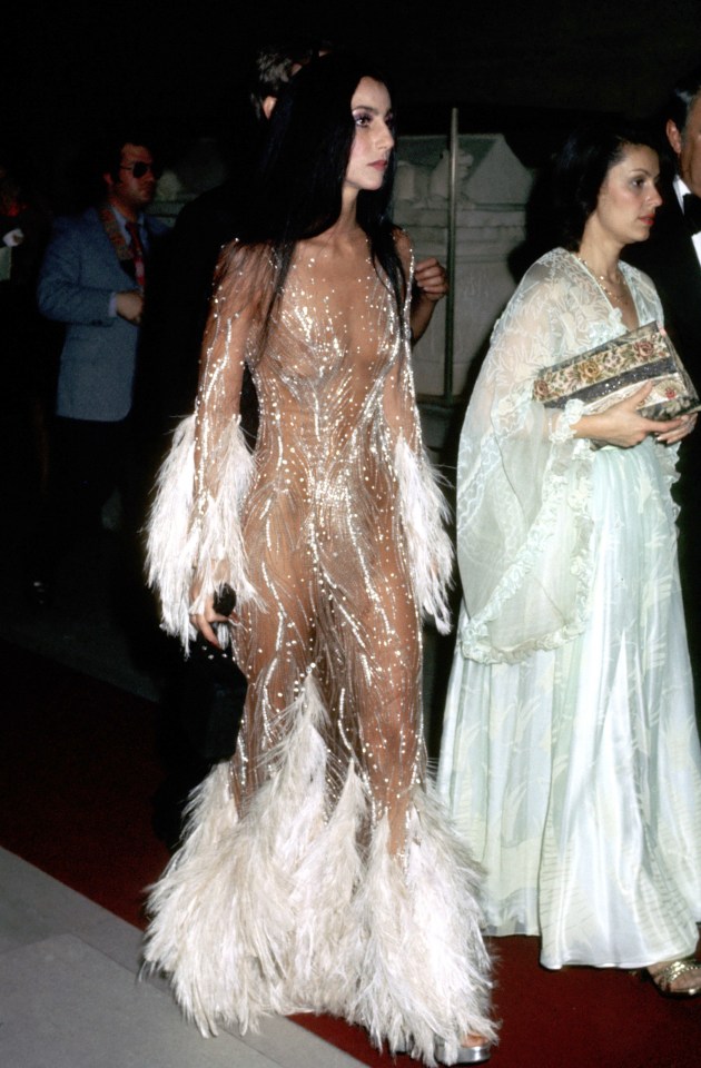 a woman in a feathered dress is walking on a red carpet