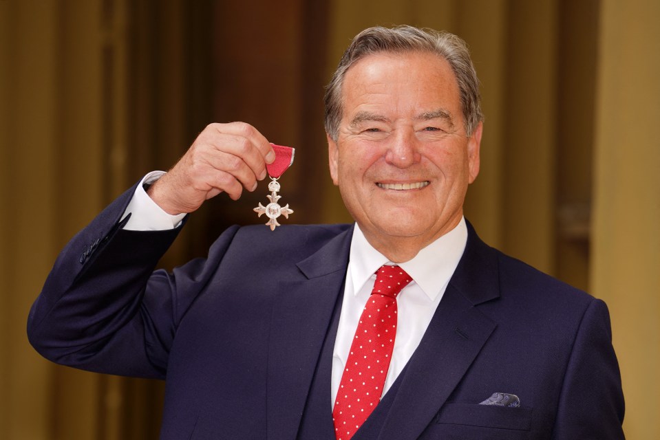 a man in a suit and red tie is holding up a medal with the letter t on it