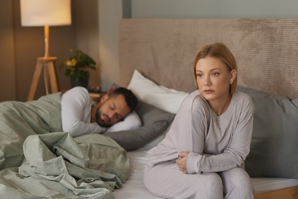 a woman sits on a bed next to a man who is sleeping