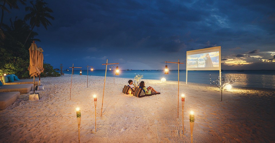 a couple sits on the beach in front of a projector screen