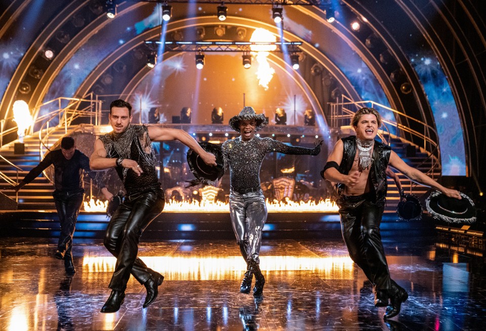 a group of men are dancing on a stage with flames in the background